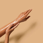 Two human hands and forearms against a warm beige background, with one hand holding the other in a smooth, polished pose that suggests skincare or cosmetic application.