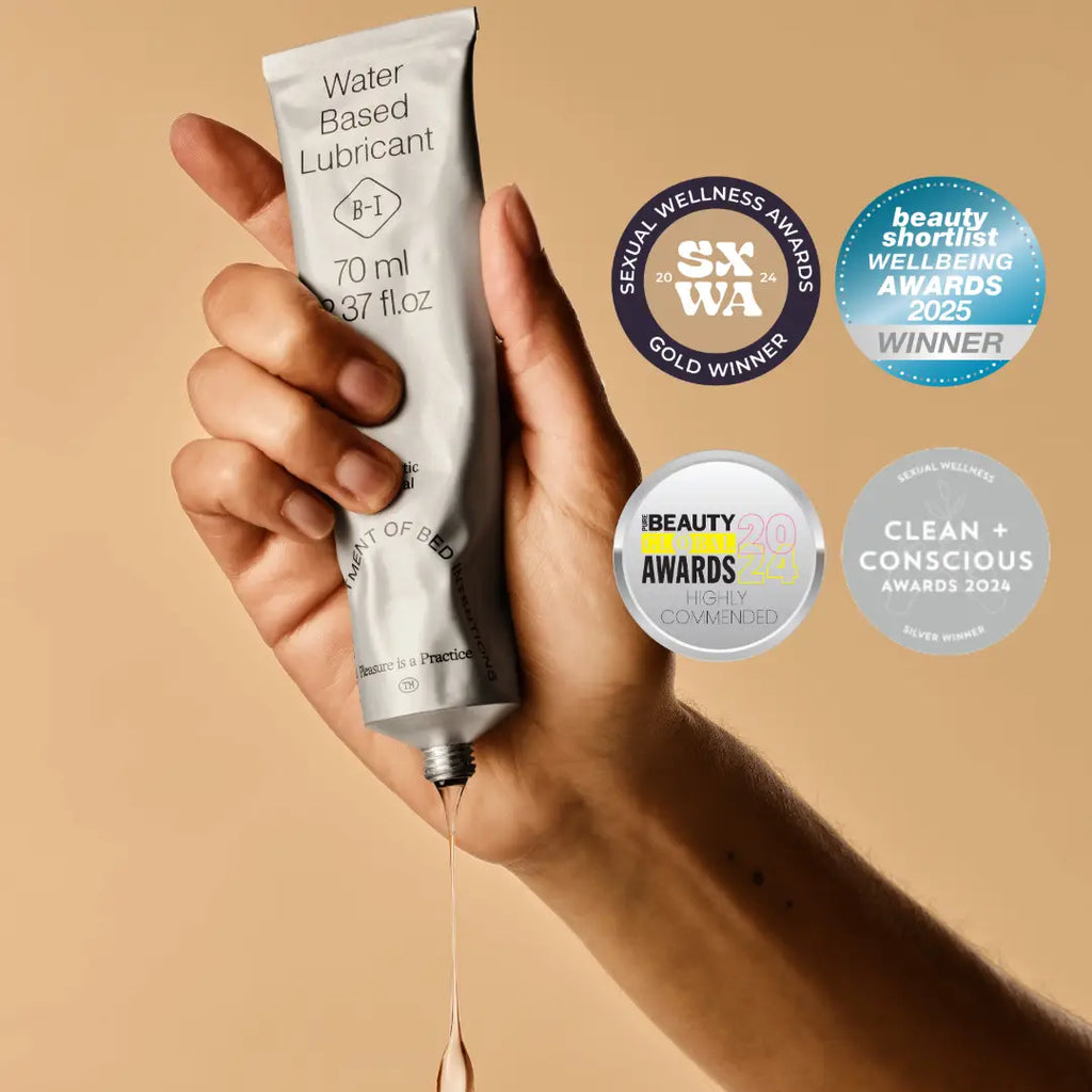 Hand holding a tube of water-based lubricant with awards on a beige background