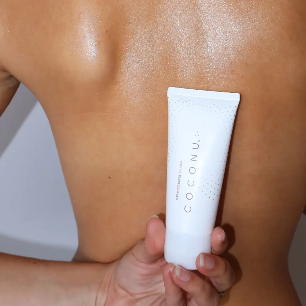 Person applying sunscreen to their shoulder with a tube labeled 'Coconut'.