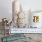 Cosmetic products including a candle, bottles, and a book on a marble surface.