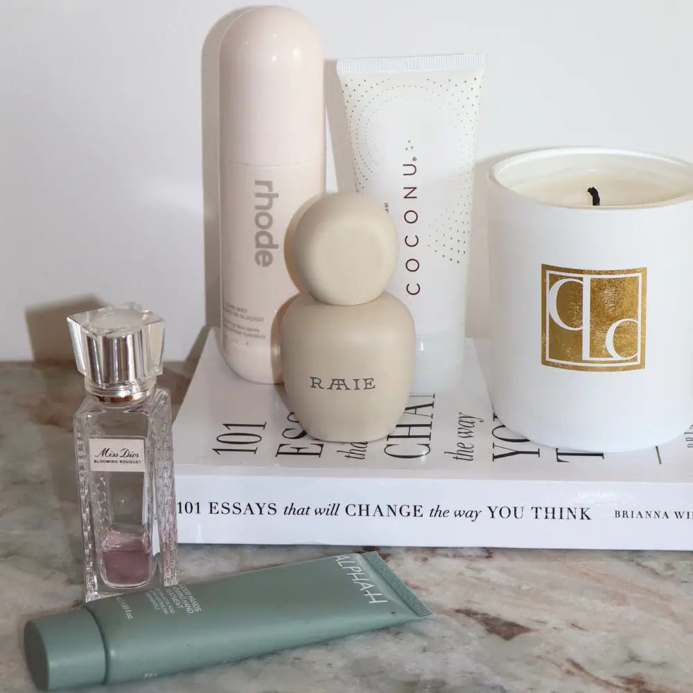 Cosmetic products including a candle, bottles, and a book on a marble surface.