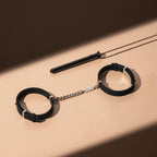 Black leather handcuffs with a chain on a beige surface