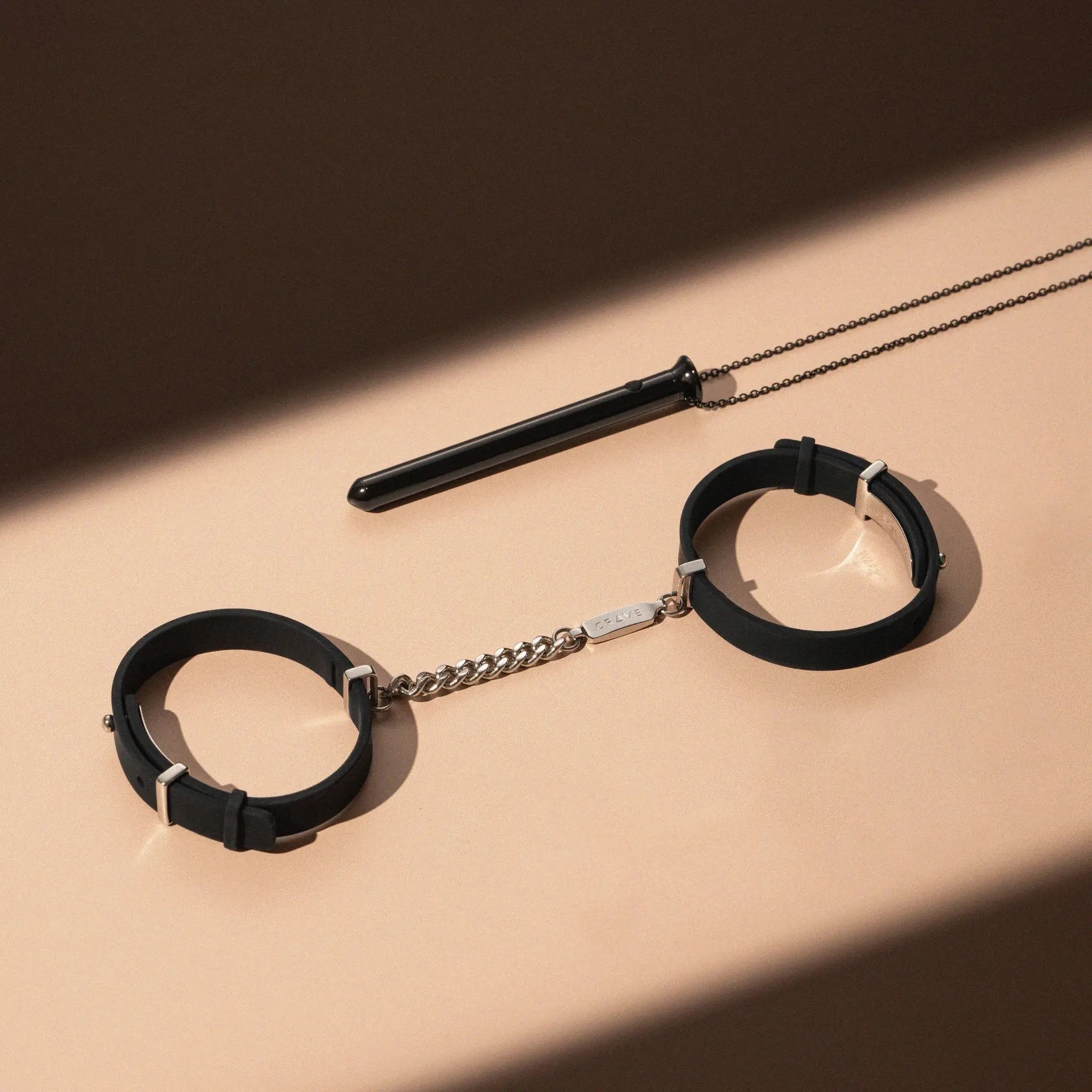 Black leather handcuffs with a chain on a beige surface