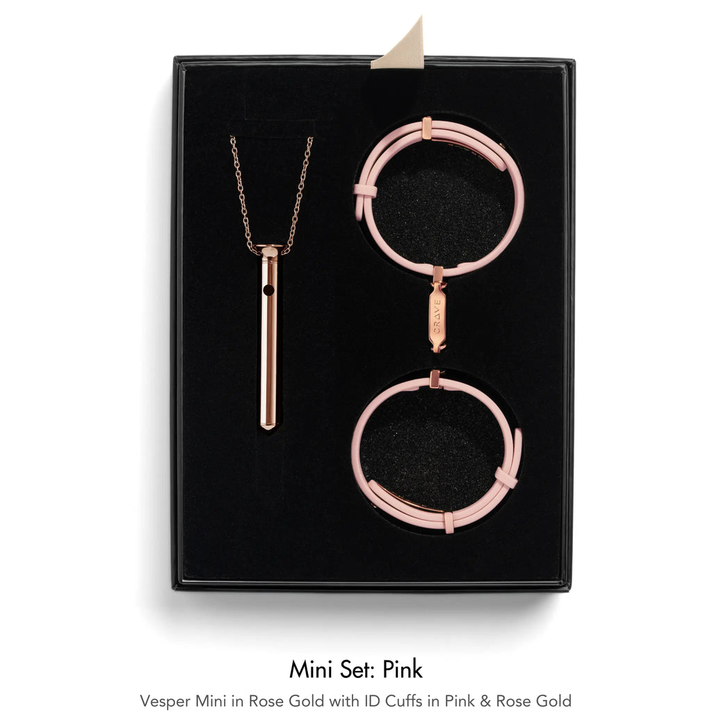 A jewelry mini set in pink and rose gold, displayed inside a black presentation box. The set includes a rose gold vesper pendant necklace, a pink ID cuff, and two rose gold ID cuffs.