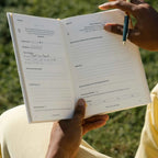 Person holding a notebook sitting outdoors.