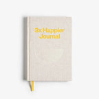 Beige journal with '3x Happier Journal' text on a white background