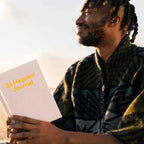 Man holding a '3x Happier Journal' against a sunset background
