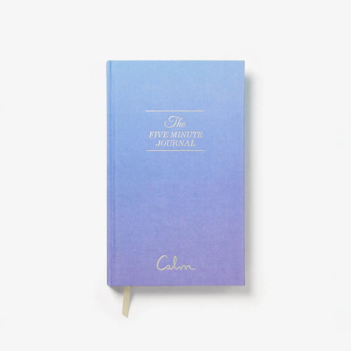 A hardcover journal with a blue-to-purple gradient cover, featuring gold foil text that reads 'The FIVE MINUTE JOURNAL' and the brand name 'Cala' near the bottom. A gold ribbon bookmark is visible at the bottom edge, set against a clean white background.