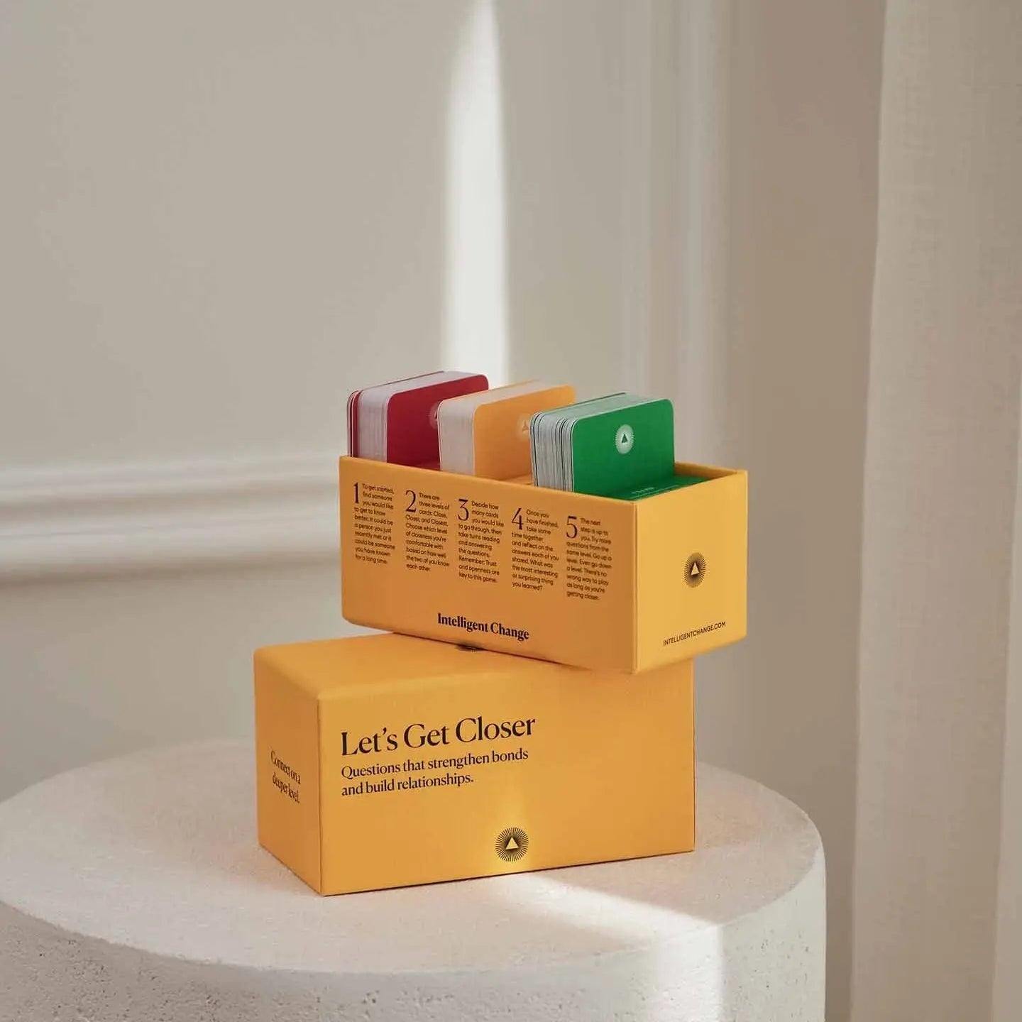 Yellow boxes with colorful cards on a white pedestal against a neutral wall.