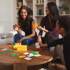 Three people playing a card game around a wooden table in a living room.