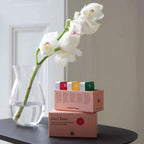 White orchid in a clear vase on a black table with boxes labeled 'Get Closer' in the background.