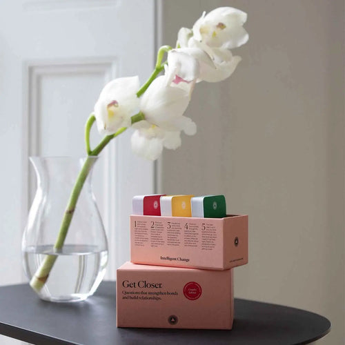 White orchid in a clear vase on a black table with boxes labeled 'Get Closer' in the background.
