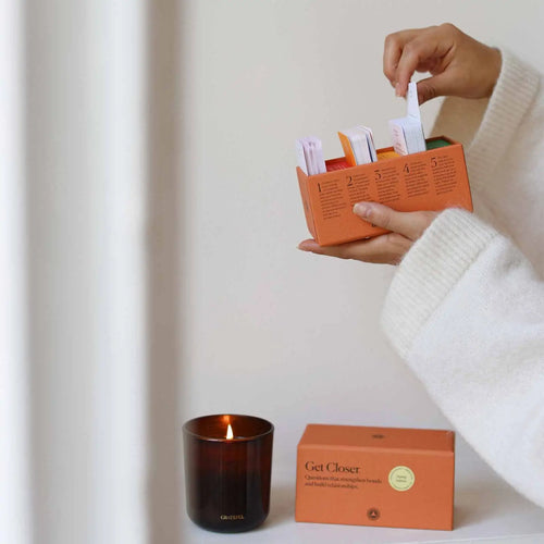 Person holding an orange box with a candle and packaging on a white surface