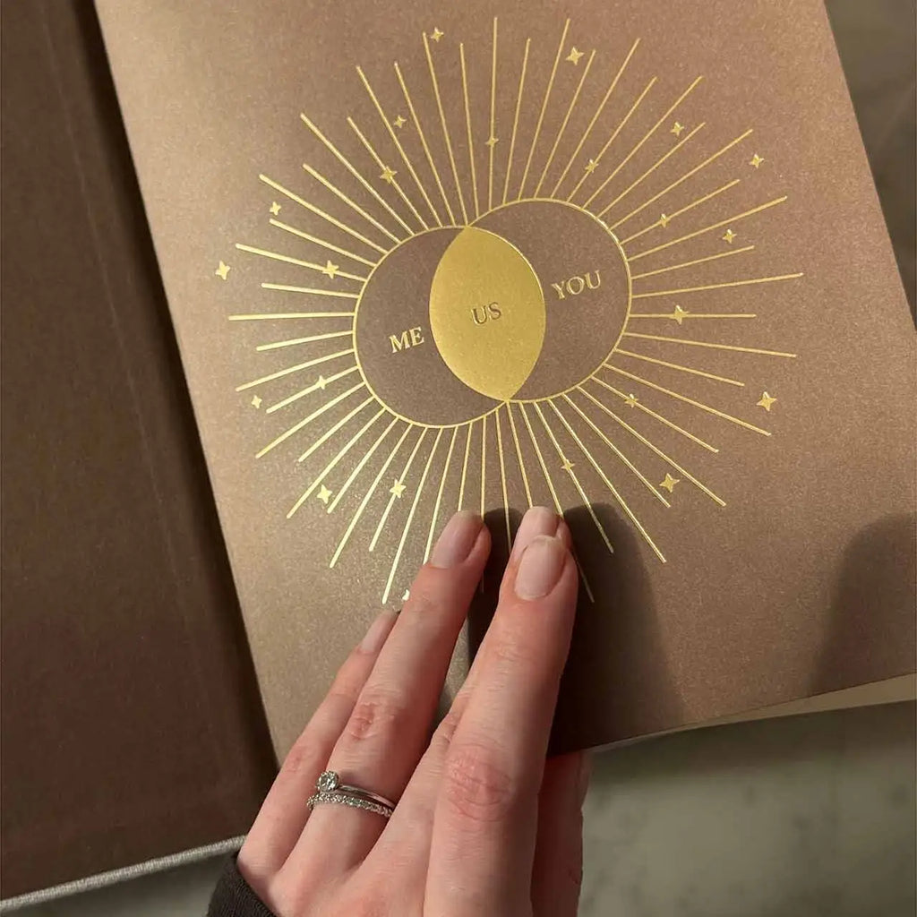 Brown book with gold 'Me Us You' design held by a hand