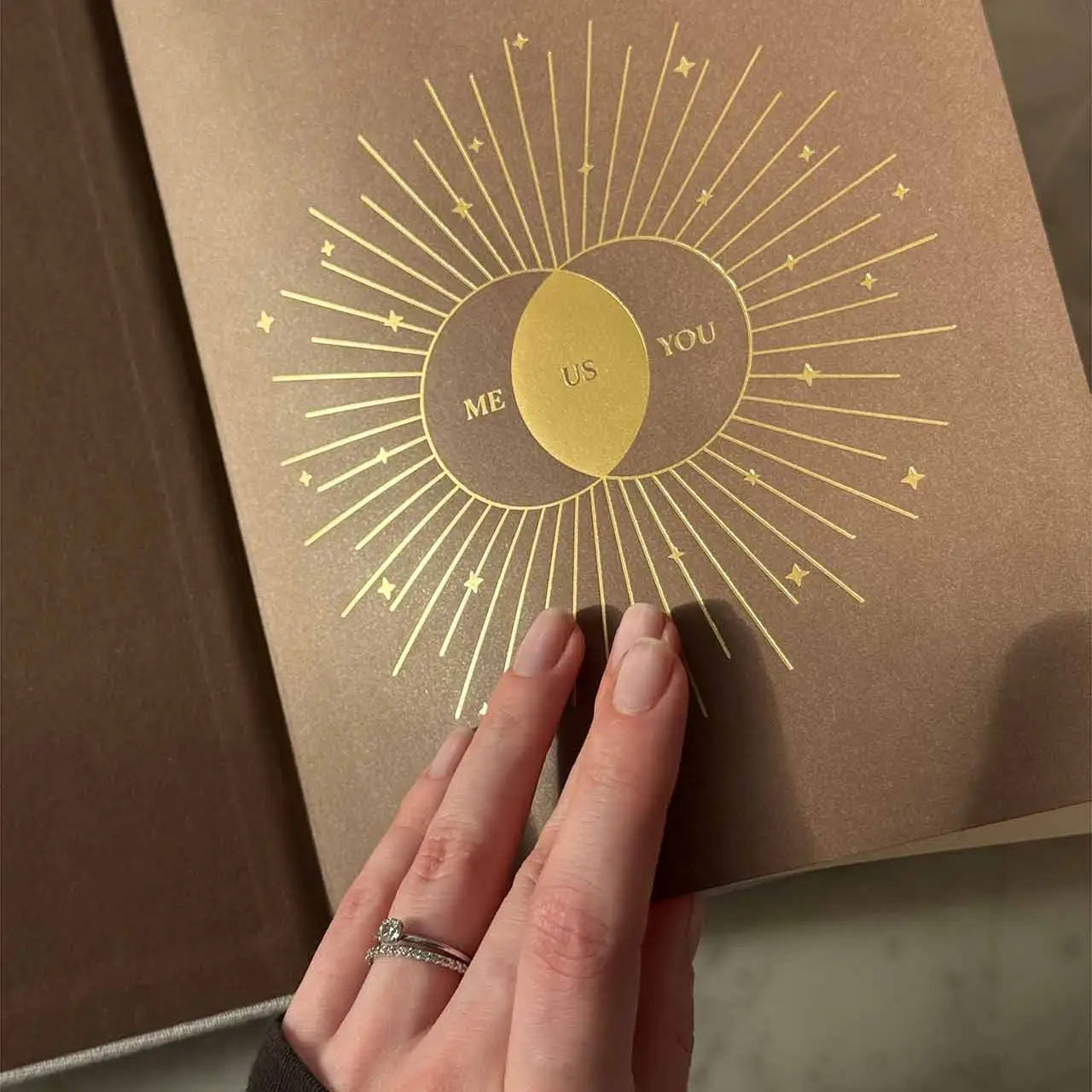 Brown book with gold 'Me Us You' design held by a hand