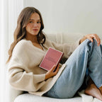 Woman sitting on a couch holding a pink book with a white background
