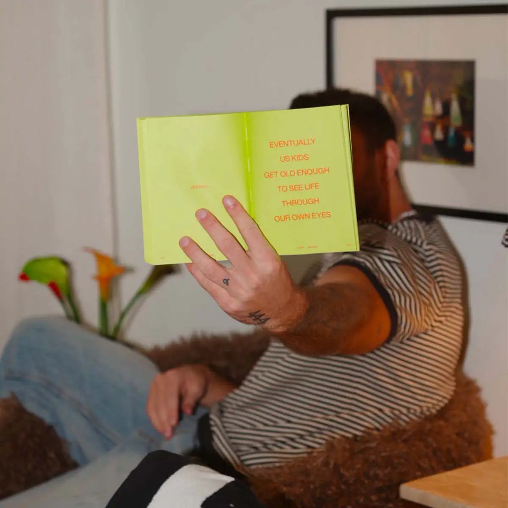 Person holding a yellow book with text, sitting on a couch in a room with decor.