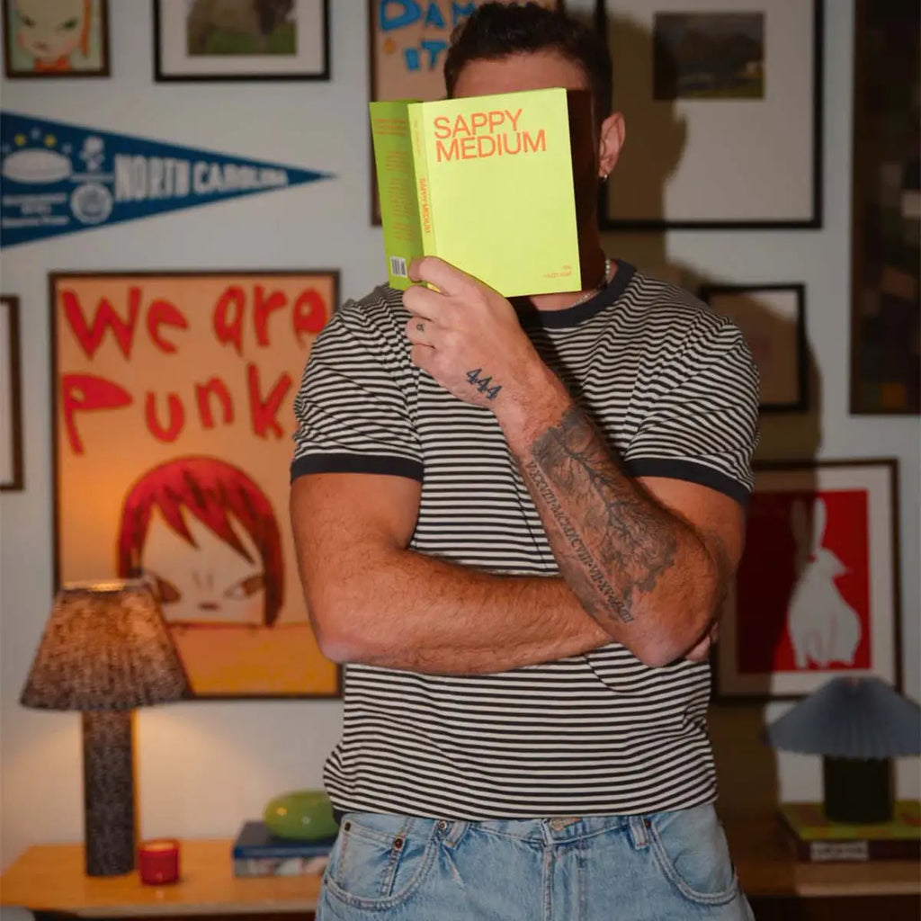 Person holding a yellow book in front of their face in a room with various posters and decor.