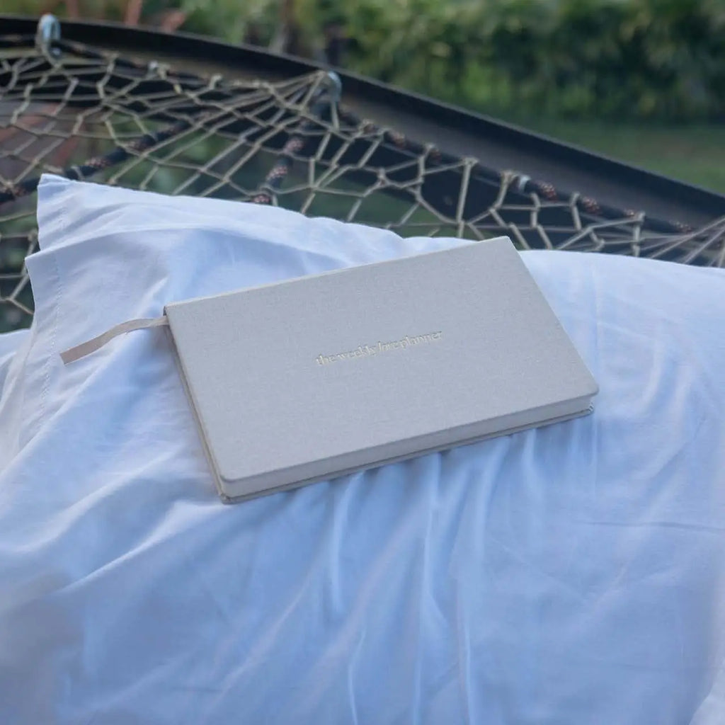Light gray notebook on a white pillow with a blurred natural background
