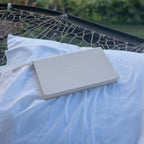Light gray notebook on a white pillow with a blurred natural background