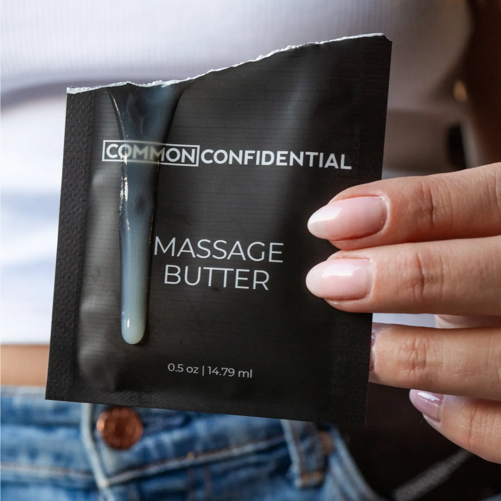 Hand holding a black package of Common Confidential massage butter.
