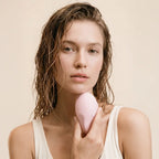 Woman holding a pink makeup sponge against a beige background