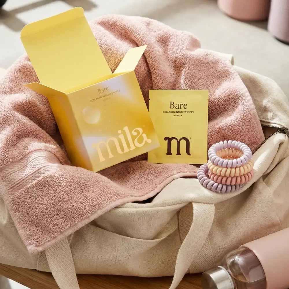 Beige bag with pink towel, yellow box, and hair ties on a wooden surface.