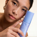 Woman holding a blue bottle with 'mila' branding against a neutral background