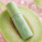 Green skincare product on a halved cantaloupe with a pink background