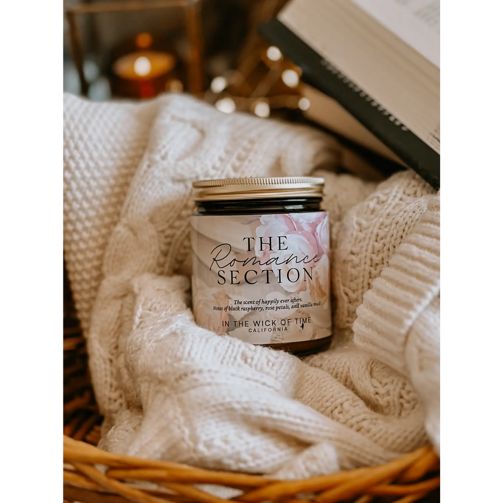 Candle labeled 'The Romance Section' in a basket with soft textures and warm tones