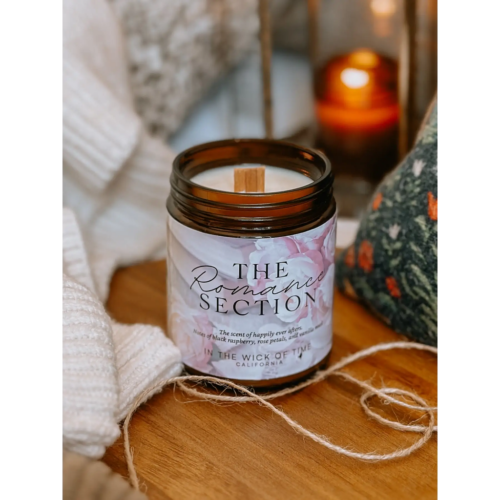 Candle labeled 'The Romance Section' on a wooden surface with soft lighting