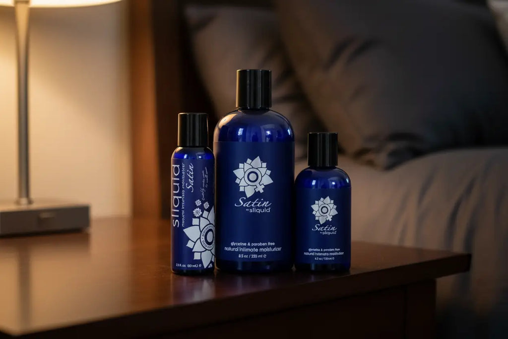 Three blue bottles with black caps on a wooden surface, with a blurred background of a lamp and pillows.