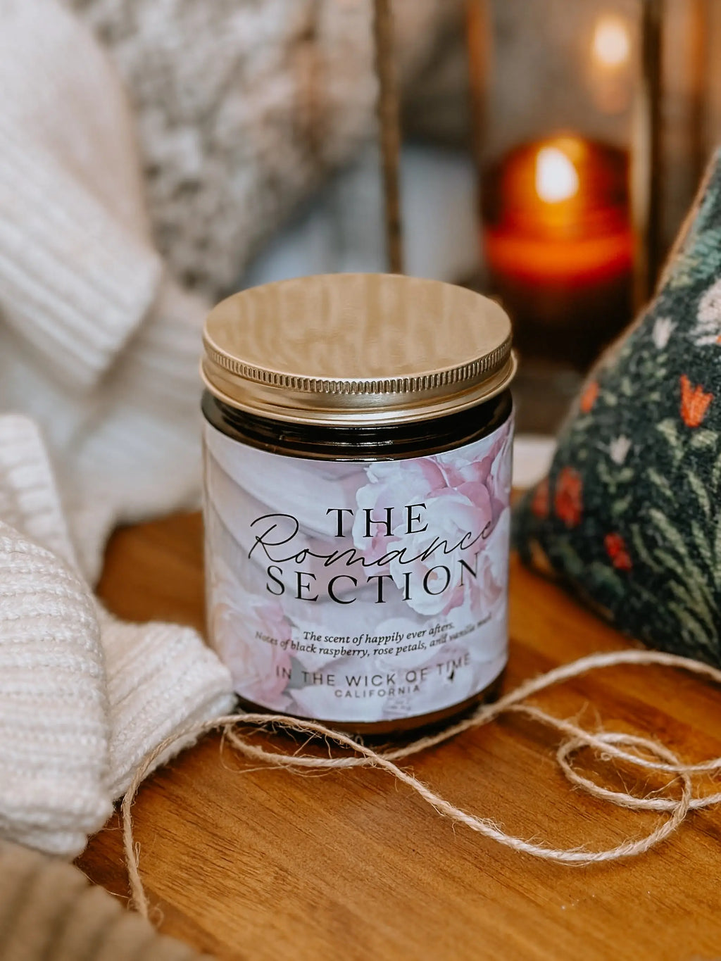 Candle labeled 'The Romance Section' on a wooden surface with soft lighting