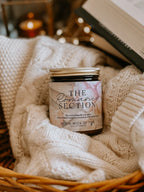 Candle labeled 'The Romance Section' in a basket with soft textures and warm tones