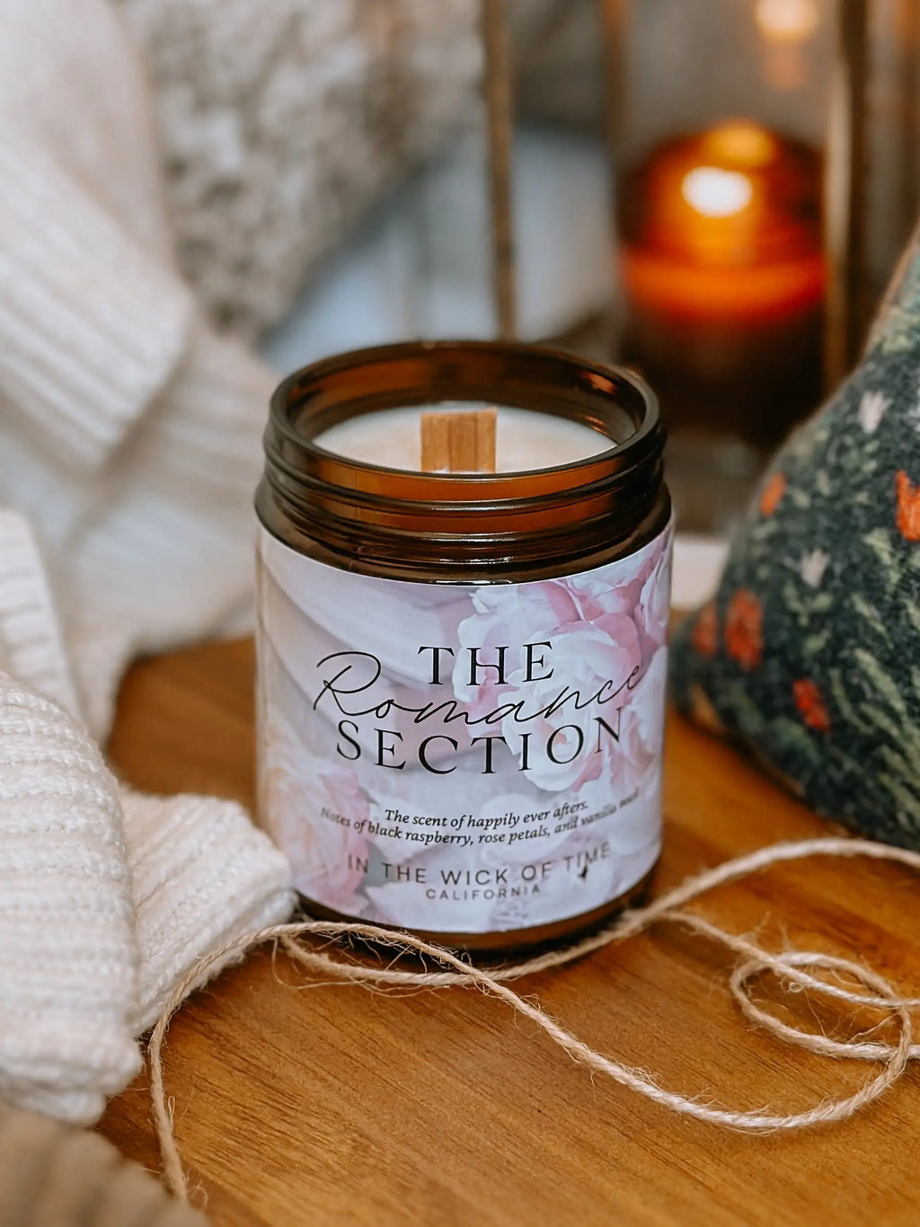 Candle labeled 'The Romance Section' on a wooden surface with soft lighting
