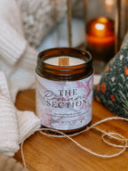 Candle labeled 'The Romance Section' on a wooden surface with soft lighting